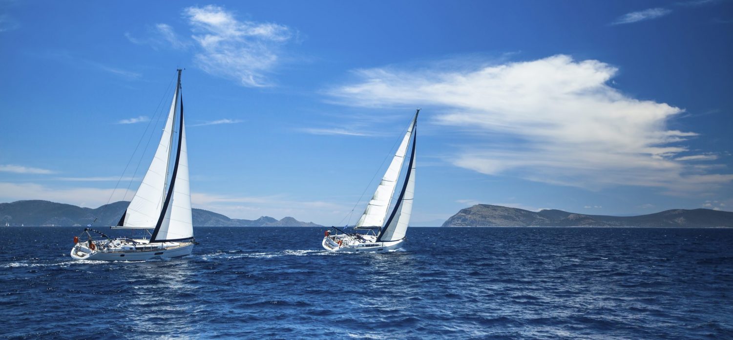 Two Sailboats sailing together in the wind through the waves at the Aegean Sea in Greece.