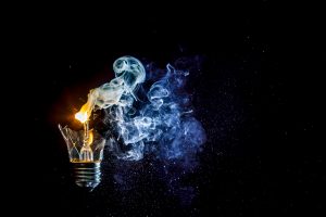 Cosmic explosion of a burning light bulb with flying splinters and smoke on a black background with a flash