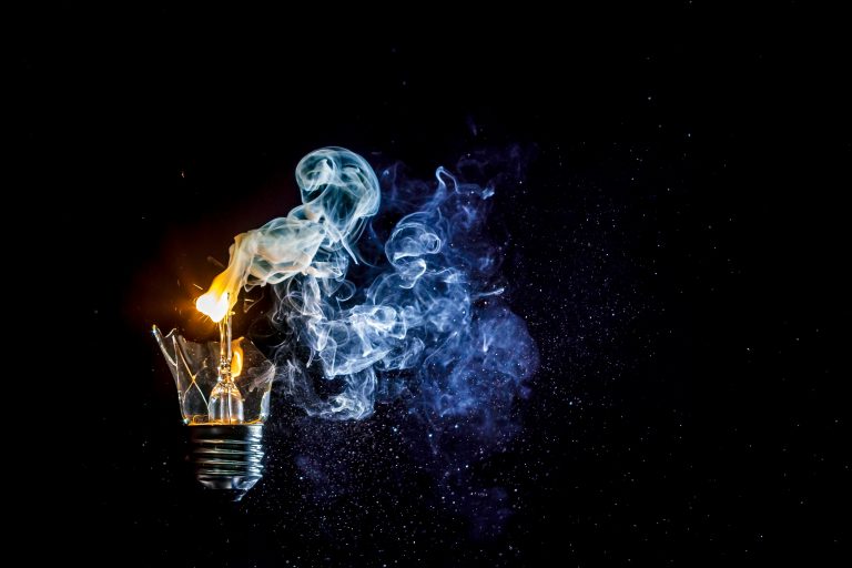 Cosmic explosion of a burning light bulb with flying splinters and smoke on a black background with a flash
