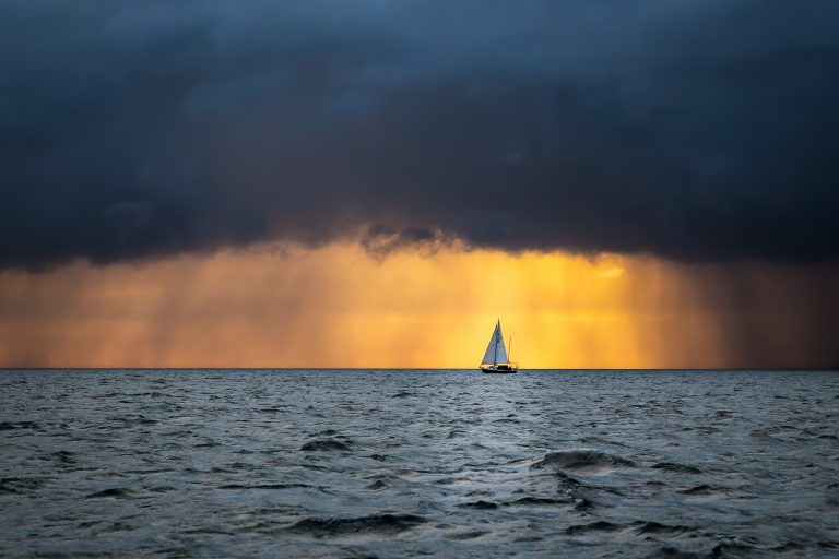 Lonely sailboat sailing in the ocean at the approaching storm and raining clouds at sunrise, English channel, near French shores